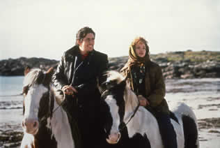 Still image of man and woman on horseback by sea